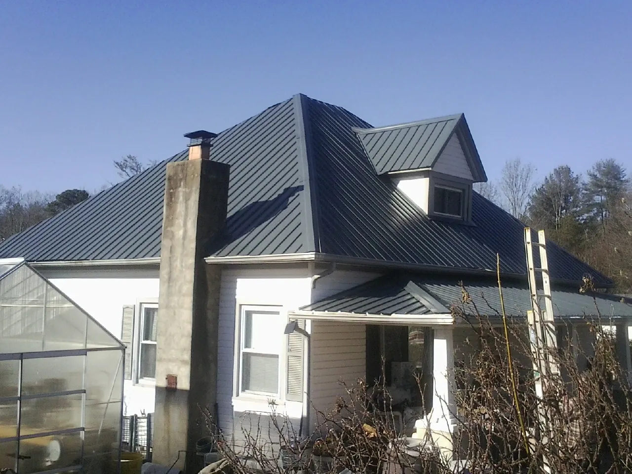 Dark blue standing seam metal roof on a white farmhouse with dormer — Slate & Tile Roof Repair by Roofing Brothers in Mc Graw