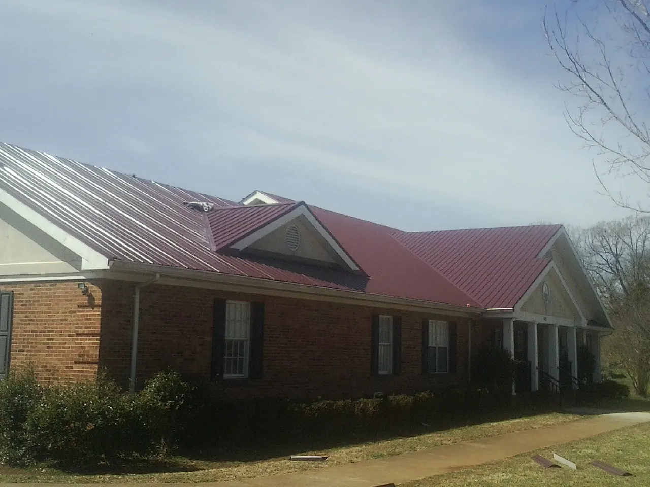Red metal roof with gabled entries on a long brick building, from a Hail Damage Roof Repair job in Mc Graw
