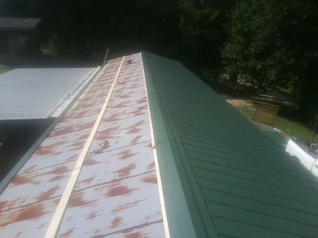 Old rusted panels beside newly installed green metal roofing — Wind Damage Roof Repair by Roofing Brothers in Mc Graw