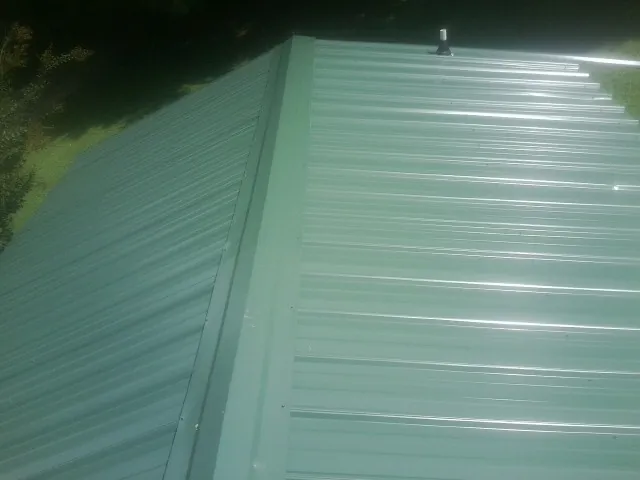 New green metal panels meeting at the ridge of a roof — Flat Roof Repair work by our crew in Mc Graw