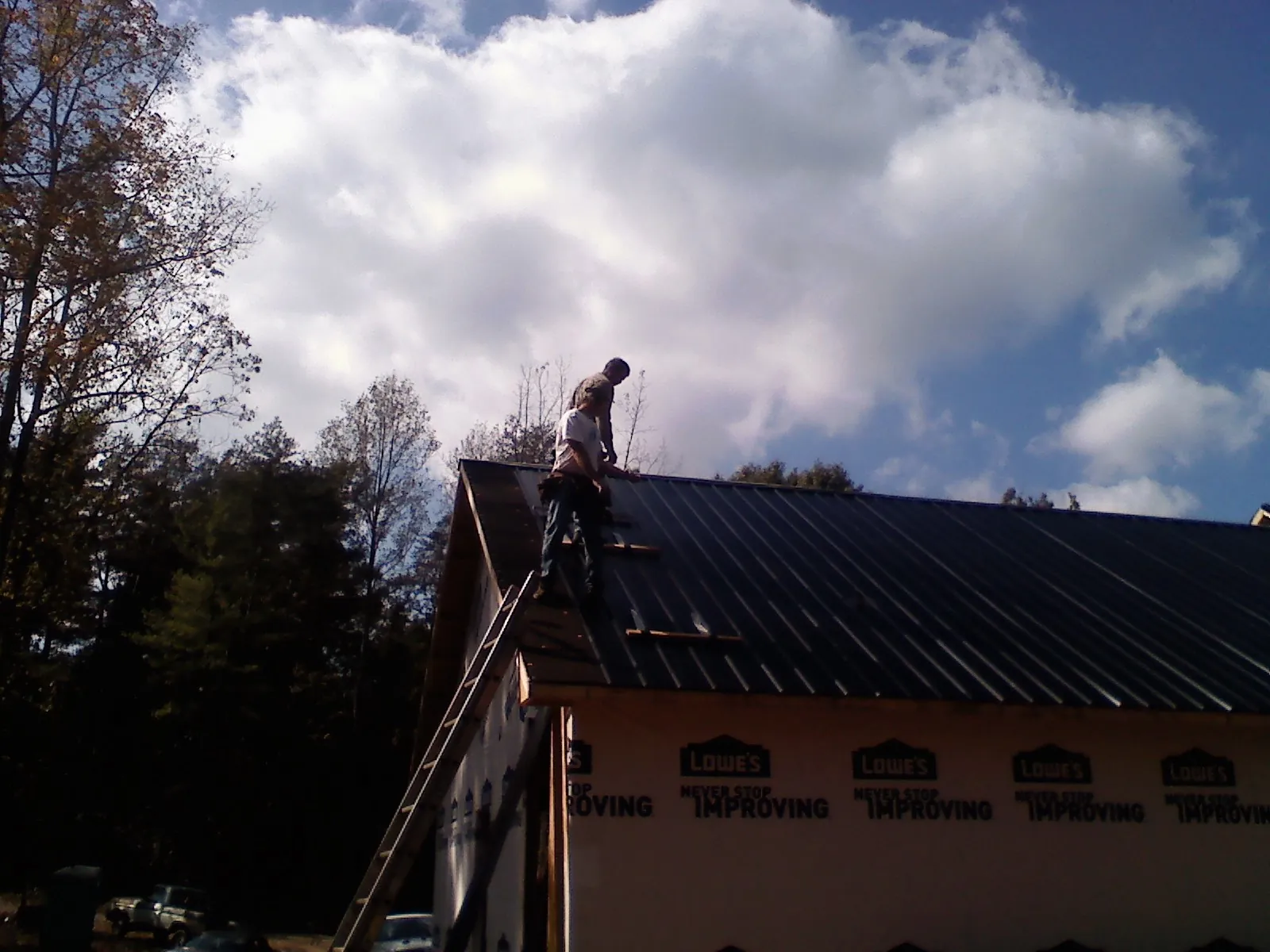 Roofer fastening dark metal panels high against a cloudy sky, from a Roof Inspection job in Mc Graw