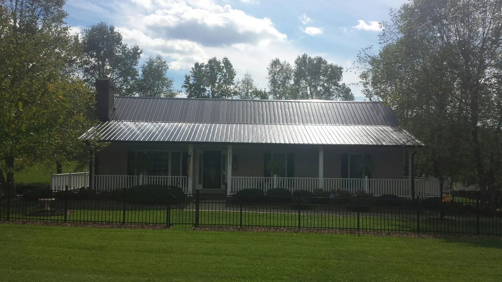 Gray metal roof on a brick ranch with a full width front porch — Gutter Guard Installation work by our crew in Mc Graw