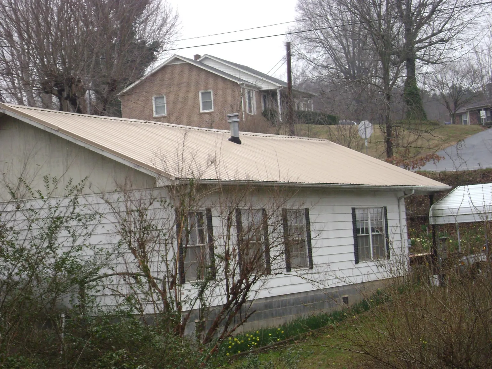 Tan metal roof on a white sided house set into a hillside — Commercial Roofing by Roofing Brothers in Mc Graw
