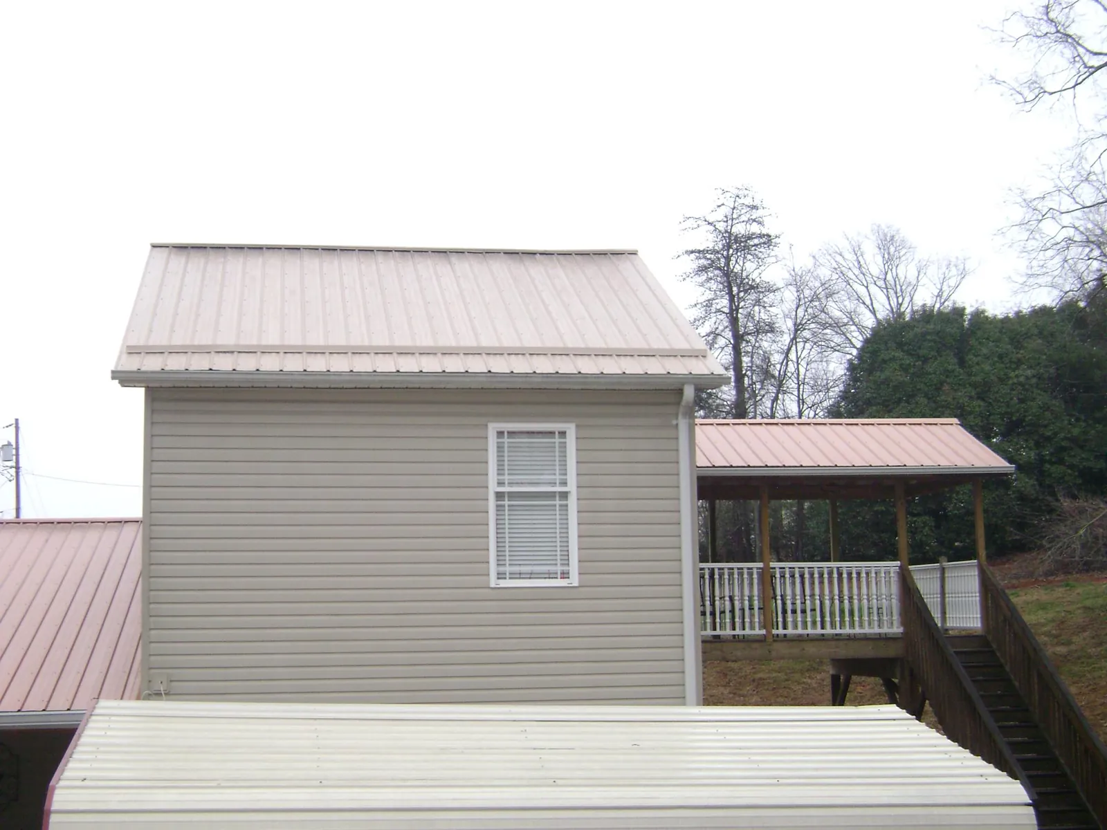 Tan metal roofs on a two story addition and attached porch, from a Roof Replacement job in Mc Graw
