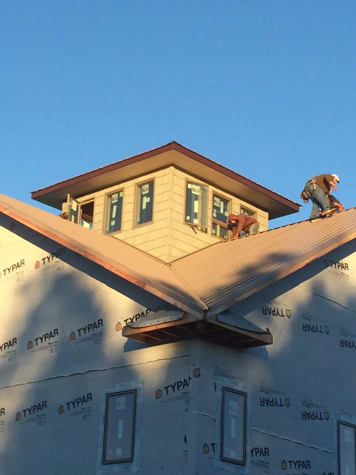 Roofers working around a rooftop cupola on a new metal roof at sunset — Roof Waterproofing in Mc Graw by Roofing Brothers
